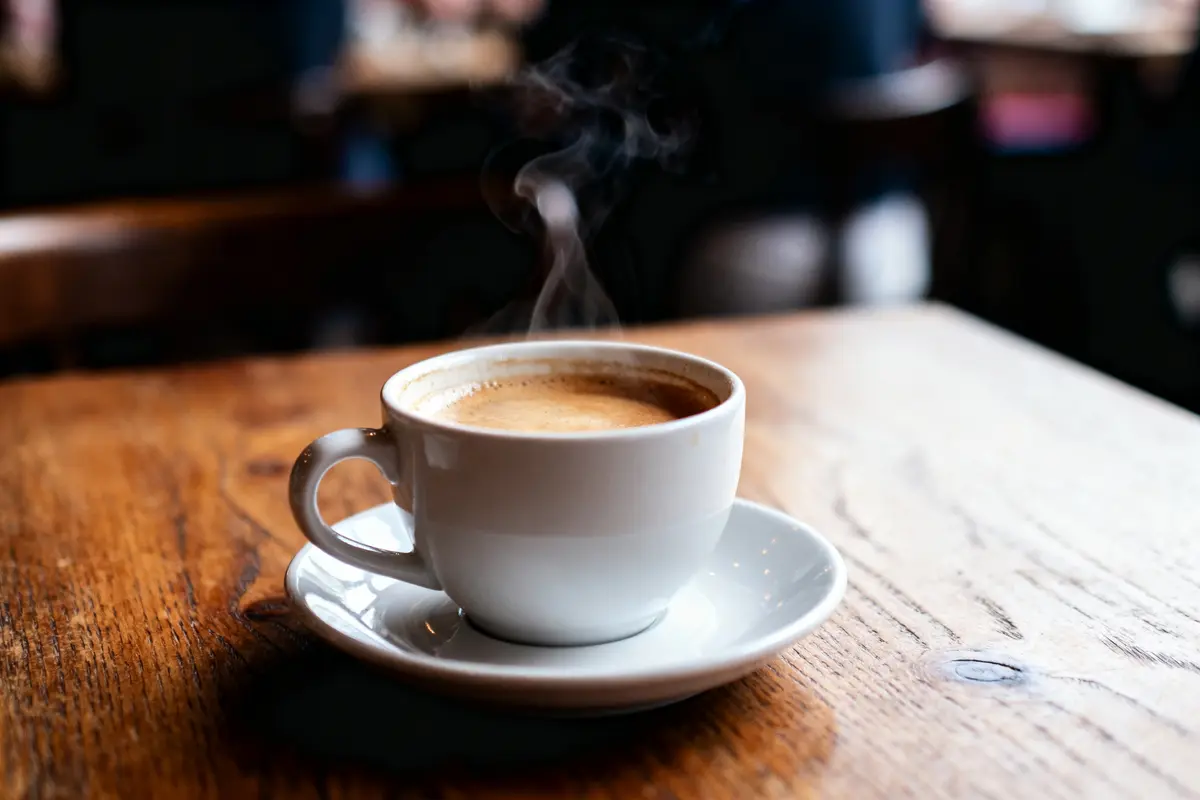 Tasse de café fumant sur table en bois, arrière-plan flou.
