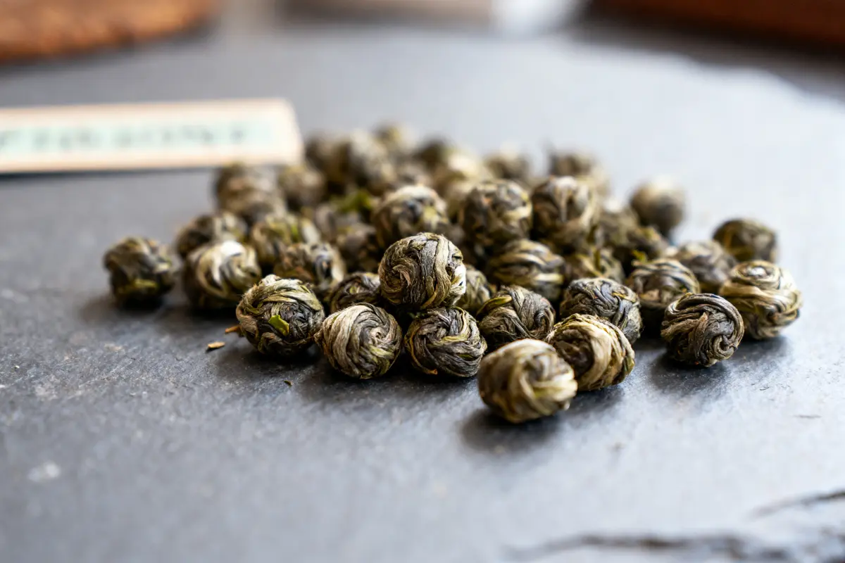 Billes de thé vert séchées sur une surface sombre, prêtes pour l'infusion.