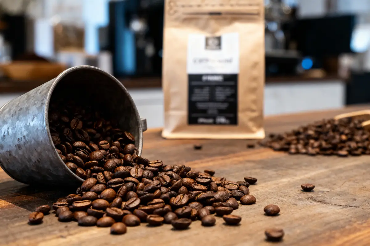 Grains de café renversés d'un seau métallique, paquet de café en arrière-plan.