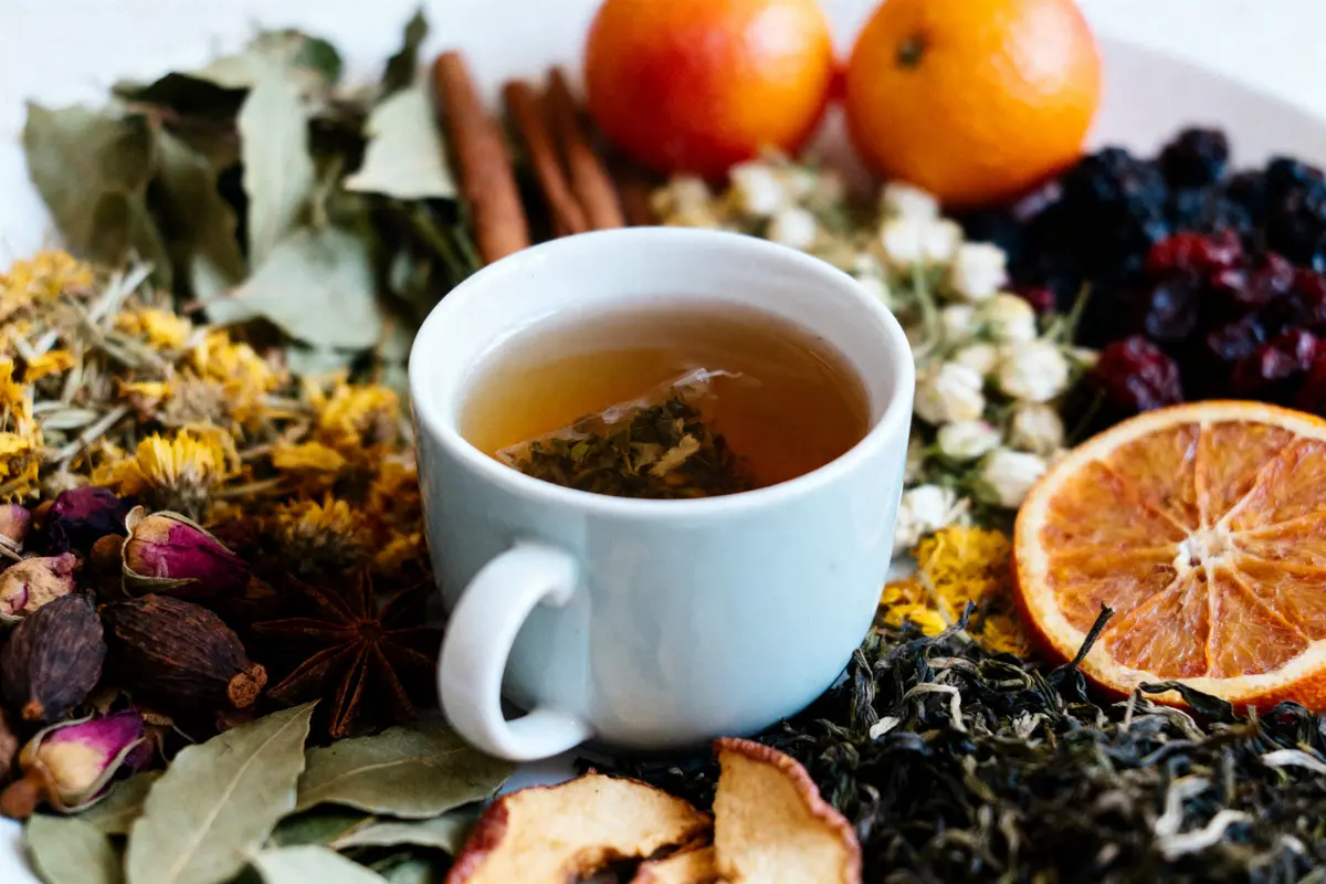 Tasse de thé entourée d'épices, herbes et agrumes variés pour infusion.