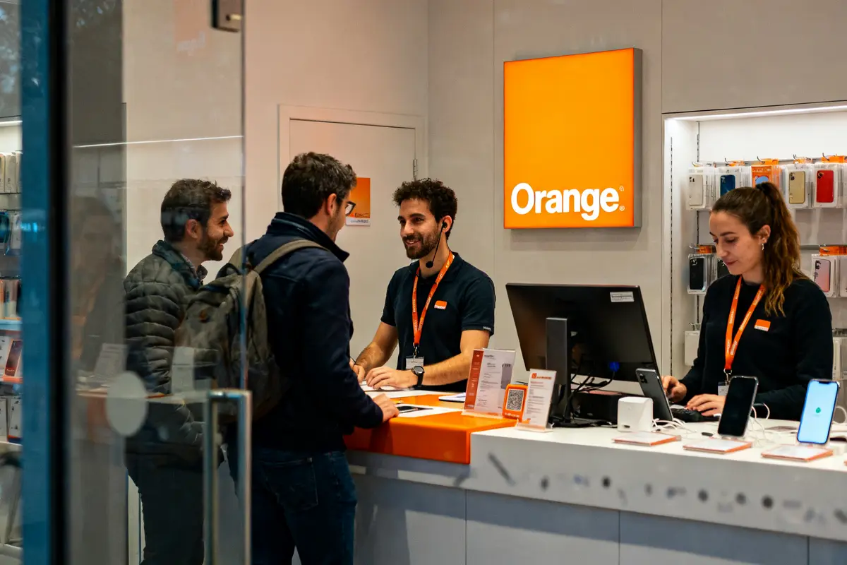 Deux clients échangent avec le personnel de la boutique Orange Versailles pour assistance mobile.