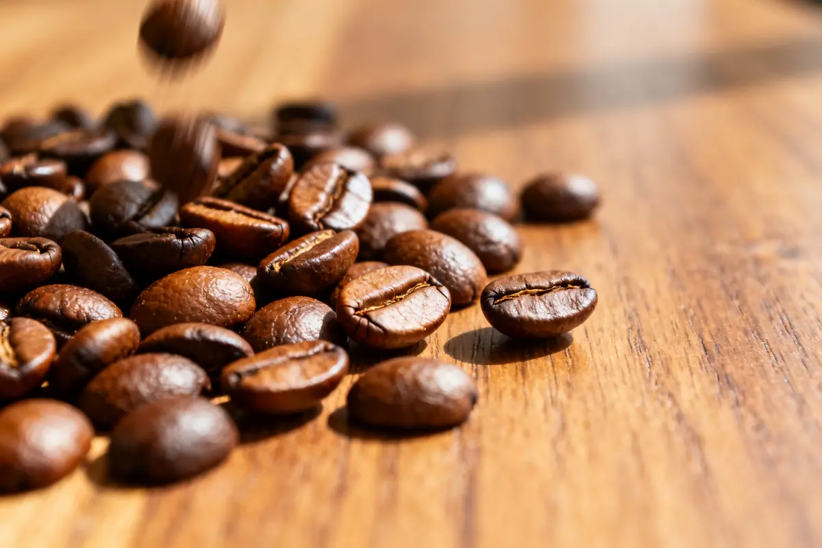 Grains de café torréfiés épars sur une table en bois éclairée par la lumière