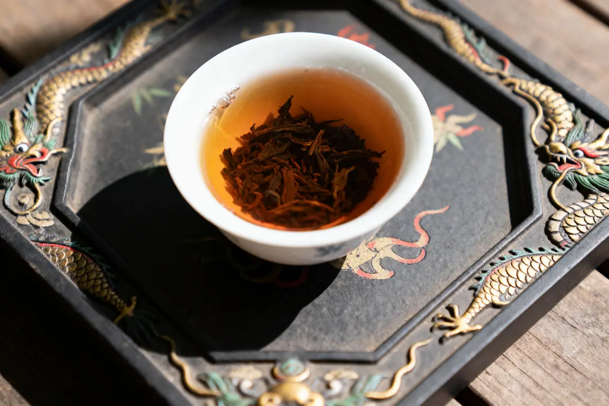 Tasse de thé sur plateau orné de dragons dorés et motifs orientaux, feuilles infusées flottant.